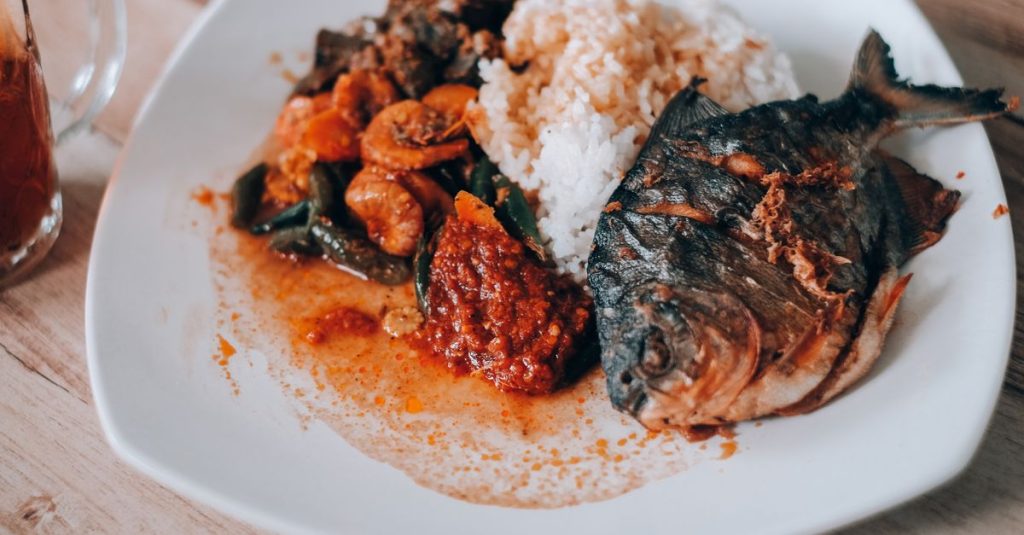 découvrez le nasi lemak, plat traditionnel malaisien savoureux à base de riz cuit dans du lait de coco, accompagné de sambal, œufs, cacahuètes, et anchois frits.
